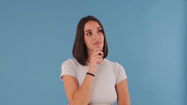 Genç bir kadın sorun üzerinde düşünür, stüdyoda mavi arka planda izole edilmiş bir şey hatırlar.