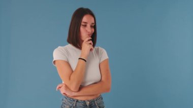 Genç bir kadın kameraya bakıyor, seçimler yapıyor, bir fikri var, stüdyoda mavi arka planda izole edilmiş.