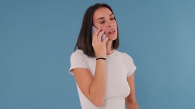 Cep telefonuyla konuşan öfkeli genç bir kadın stüdyoda mavi arka planda izole edilmiş.