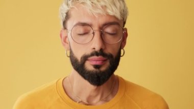 Adamın gözlerini açtığı ve sarı arka planda izole edilmiş bir gülümsemeyle kameraya baktığı yakın plan.