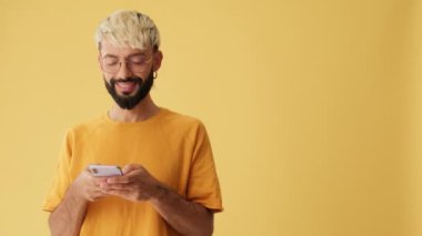 Elinde cep telefonu olan gülümseyen bir adam sarı arka planda izole bir şekilde baş parmak gösteriyor.