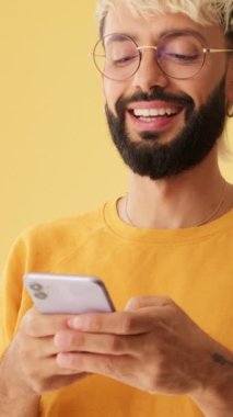 Yakın plan, erkekler SMS okurken güler, cep telefonundan video izlerler, sarı arka planda izole olurlar.