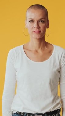 Genç kadın, stüdyoda sarı arka planda izole edilmiş kameraya bakarak zafere seviniyor.