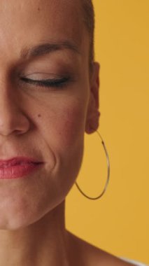 Bir kadının yüzünün yarısı, gözlerini açar ve sarı arka planda izole edilmiş kameraya bakar.