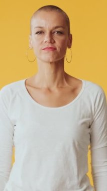 Stüdyoda sarı arka planda izole edilmiş kameraya bakan genç bir kadın.