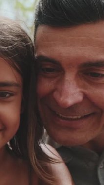 Yakın çekim, mutlu aile akıllı telefon kullanarak parktaki bankta oturan resimlere ve videolara bakıyor.