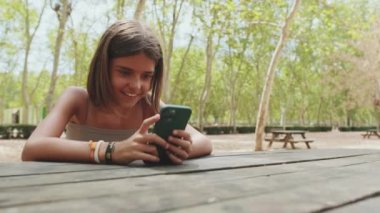 Parkta otururken cep telefonu kullanan gülümseyen genç kız.