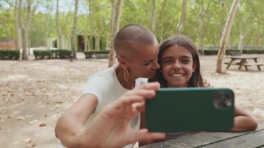 Mutlu anne genç kızını öpüyor ve cep telefonuyla selfie çekiyor.