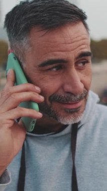 Yakın plan, spor kıyafetli orta yaşlı adam köprüde dururken cep telefonuyla konuşuyor.