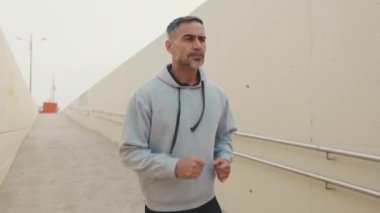 Spor giyimli orta yaşlı bir adam dışarıda koşuyor.