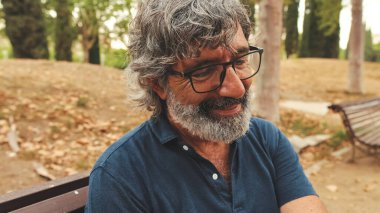 Parktaki bankta dinlenen, gülümseyen yaşlı adama yakın plan.