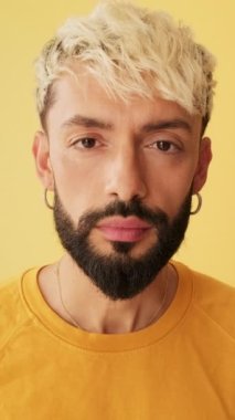 Kameraya aynada bakar gibi bakan bir adam. Stüdyoda sarı arka planda gözlüklerini ayarlıyor.