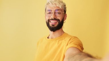 Kameraya bakan adamın yakın plan görüntüleri, stüdyoda izole edilmiş sarı arkaplanda el sallaması.