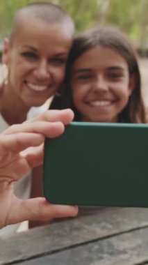 Mutlu anne genç kızını öpüyor ve cep telefonuyla selfie çekiyor.