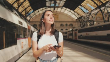 Güzel kız gezgin tren istasyonunun peronunda dururken cep telefonu kullanıyor.