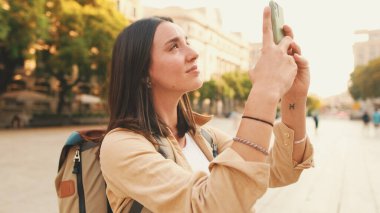 Omuzlarında sırt çantasıyla gezgin bir kız Avrupa 'nın tarihi bölgesindeki eski bir binanın cep telefonuyla fotoğraf çekiyor.