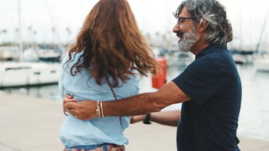 Mutlu orta yaşlı çift yat arka planında marinada güvenle dans ederken gülümsüyor.