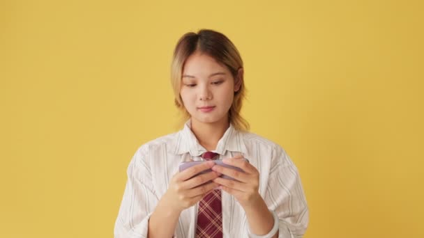 スタジオで黄色の背景に隔離された携帯電話でオンラインゲームをしている若い女性 — ストック動画