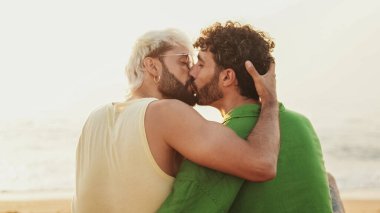 Genç eşcinsel çiftin sahilde oturup, gülüşmeleri, konuşmaları ve öpüşmeleri yakın plan.