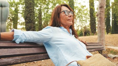 Güzel, gülümseyen, gözlüklü emekli kadın parkta otururken dinleniyor.