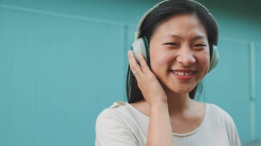 Kulaklık takmış, günlük giysiler giymiş, müzik dinleyip şarkı söyleyen güzel bir esmer kız.