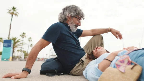 Happy middle aged couple, retired elderly couple enjoy joint outdoor recreation, relax and chat lying on pier on yacht background