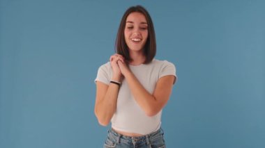 Gülümseyen kadın kameraya bakıyor. Avuçlarını katlıyor. Stüdyoda mavi arka planda çok yalnız.