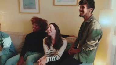 Arkadaşlar rahat bir oturma odasında kanepede otururken birlikte eğlenir, güler ve eğlenirler.