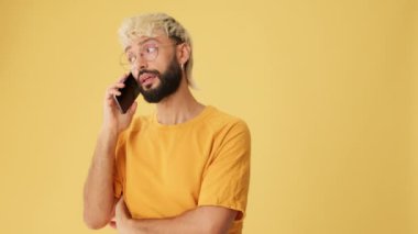 Cep telefonundan konuşan bir adam, stüdyoda sarı arka planda izole edilmiş.