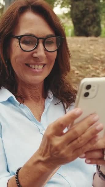 Vacker Äldre Kvinna Glasögon Med Telefon Medan Sitter Parken — Stockvideo