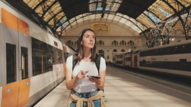 Güzel kız gezgin tren istasyonunun peronunda dururken cep telefonu kullanıyor.