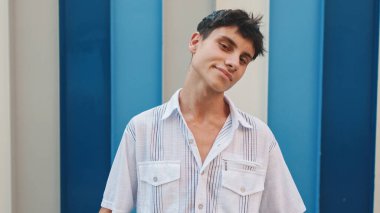 Kapalı, sıradan kıyafetler giymiş bir adam çizgili arka plandaki kameraya bakıyor.