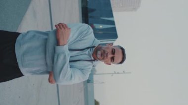 Dikey video, spor kıyafetli orta yaşlı bir adam kollarını kavuşturup kameraya bakıyor ve caddede duruyor, kamera ileri doğru hareket ediyor.