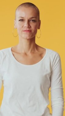 Gülümseyen genç bir kadın kollarını kavuşturup stüdyoda sarı arka planda izole edilmiş kameraya bakıyor.