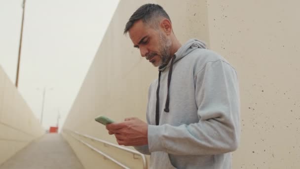 穿着运动服的中年男子在训练后在手机上输入短信息 — 图库视频影像