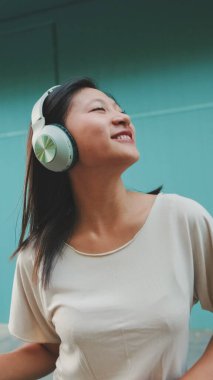 Kulaklık takmış, müzik dinleyen ve mavi duvarda dans eden mutlu, güzel esmer kız.