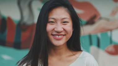 Güzel, mutlu esmer kız, günlük giysiler içinde kameraya bakıp gülüyor.