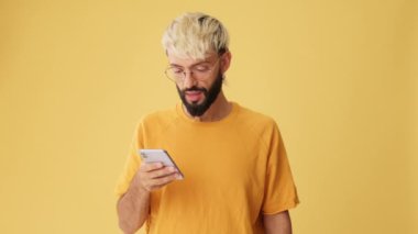 Telefonu elinde iyi haberler getiren, zaferi kutlayan, sarı arka planda izole edilmiş bir adam.
