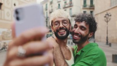 Eşcinsel çift ayağa kalkar ve cep telefonundan video görüşmesi yapar, selamlaşarak el sallarlar