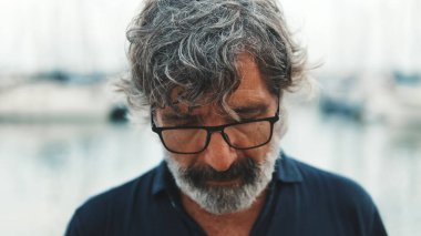 Gözlüklü son sınıf öğrencisinin limanda dikilip yatların arka planına baktığı yakın plan.