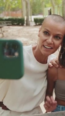 Parktaki bankta oturan fotoğraf ve videolara bakarak akıllı telefon kullanan mutlu bir aile.