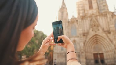 Omuzlarında sırt çantasıyla gezgin bir kız Avrupa 'nın tarihi bölgesinde, arka manzaralı eski bir binanın cep telefonuyla fotoğraf çekiyor.