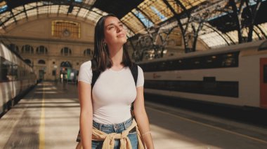 Güzel gezgin kız tren istasyonunun platformunda yürüyor.