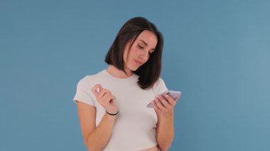Genç bir kadın cep telefonu kullanıyor. Stüdyonun mavi arka planında izole edilmiş bir şekilde kayıyor.