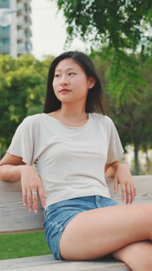 Güzel esmer kız şehir parkındaki bankta oturmuş etrafa bakıyor.