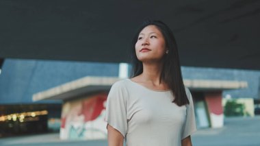 Güzel, mutlu esmer kız günlük giysiler içinde şehirde yürüyüş yapıyor ve yaz gününün tadını çıkarıyor.