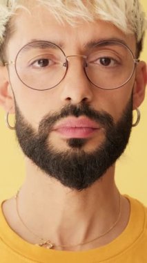 Stüdyoda sarı arkaplanda izole edilmiş kameraya bakan adamın yakın çekimi.