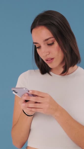 利用蓝色背景的孤立无援的手机 惊喜若狂地赢得了美丽的年轻女子的支持 — 图库视频影像