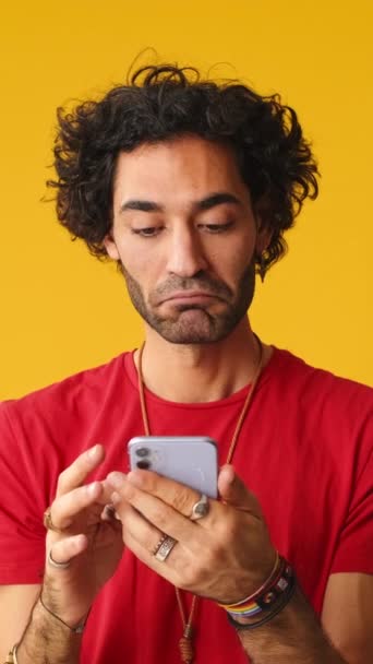 携帯電話を使用して笑顔の男 スタジオで黄色の背景に単離されたアプリケーションをスクロール — ストック動画