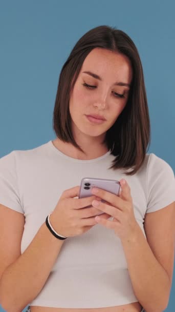 Молода Жінка Тримається Допомогою Мобільного Телефону Ізольовано Синьому Фоні Студії — стокове відео